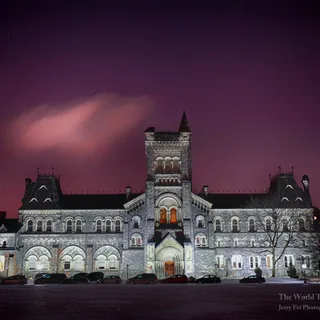 University College at the University of Toronto on a winter night, with its illuminated stone facade, central tower, and arched windows above snow-covered grounds beneath a purple sky.