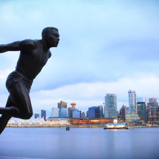 Bronze Harry Jerome runner statue in Stanley Park, with Coal Harbour, Canada Place’s white sails, and Vancouver’s illuminated waterfront skyline behind it.