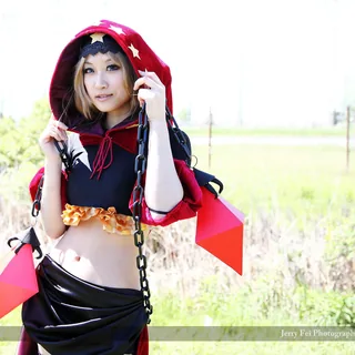 Yume portraying Velvet from Odin Sphere, holding a gold-starred red hood with red crystal props hanging from black chains beside a black-and-red costume.