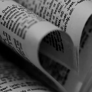 An open dictionary with two pages curled inward to form a heart beside the word “love,” photographed in black and white.